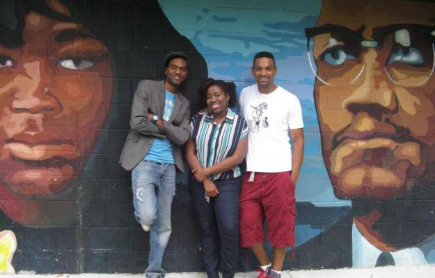Three people standing in front of a mural of Malcolm X in the eponymous Philly park.