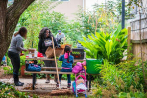 A group of people sit on a bench in a garden. 