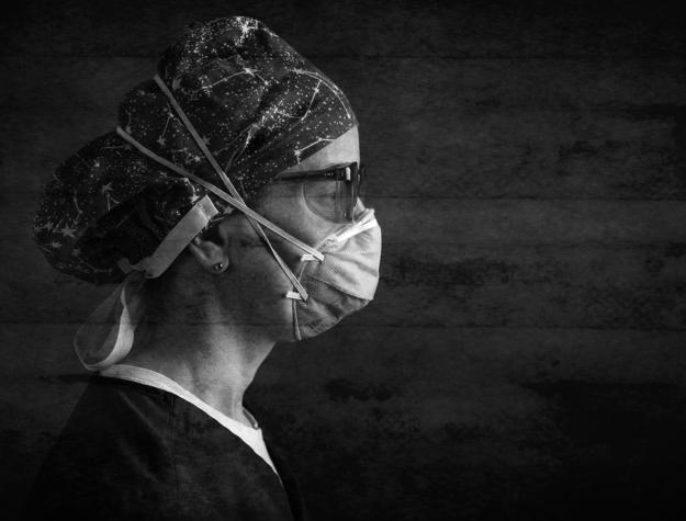 A woman wearing a N95 mask and glasses in profile.