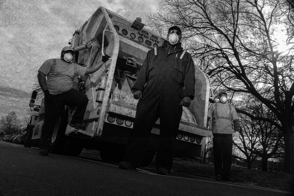 Three people stand around a trash truck on a city street.