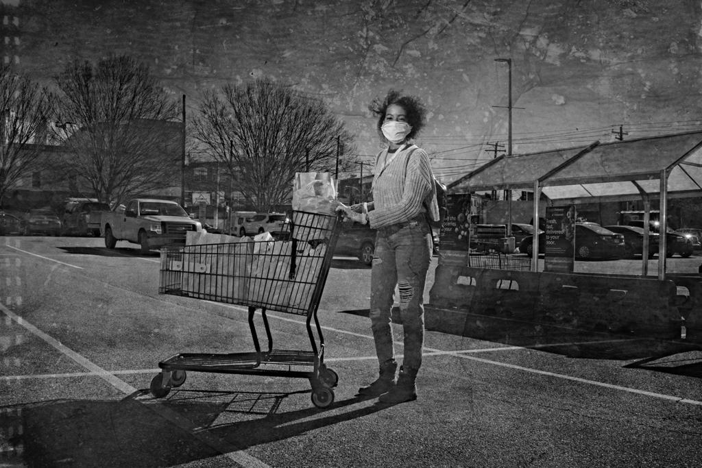 A woman pushing a shopping cart through a parking lot.