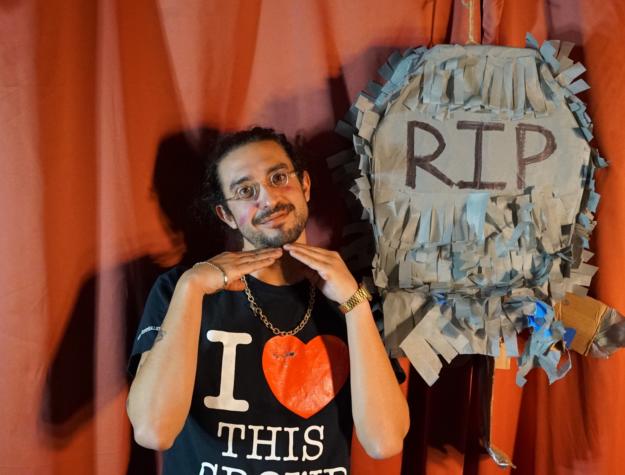 Comedian Dave Wasserman poses like an adorable child in front of a paper machete gravestone.
