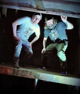 DJs Willyum and Rob Paine standing on an industrial platform at a show.