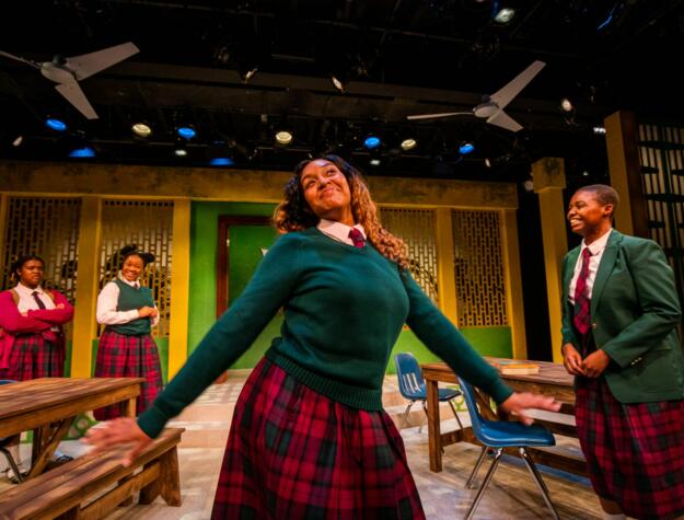 Young Black girls in school uniforms on stage rehearsing.