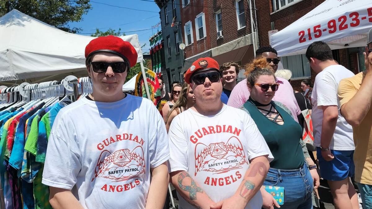 Two men in Guardian Angels shirts, including TJ Cahill, wearing berets at a South Philly community event. They are wearing sunglasses, too, and posing tough.