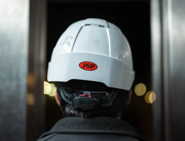 Close-up of an industrial worker wearing a JSP safety helmet at night, viewed from behind. (stock photo via Pexels)